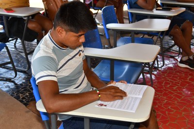 Rapaz indígena lendo cartilha bilíngue.